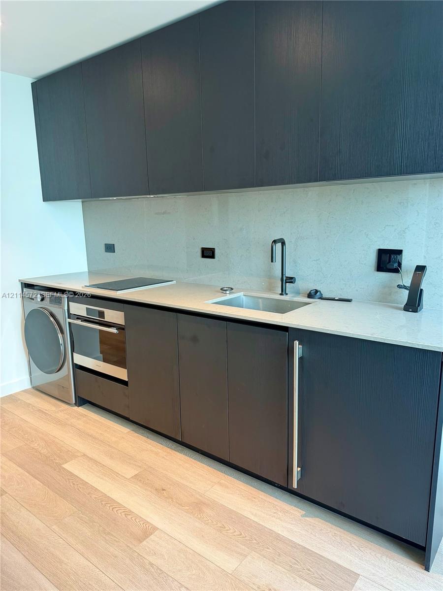 Modern cabinetry with flat-panel doors, light-toned stone-finish countertops, integrated stainless steel appliances, under-mount sink with matte black faucet, and wide-plank wood-finish flooring