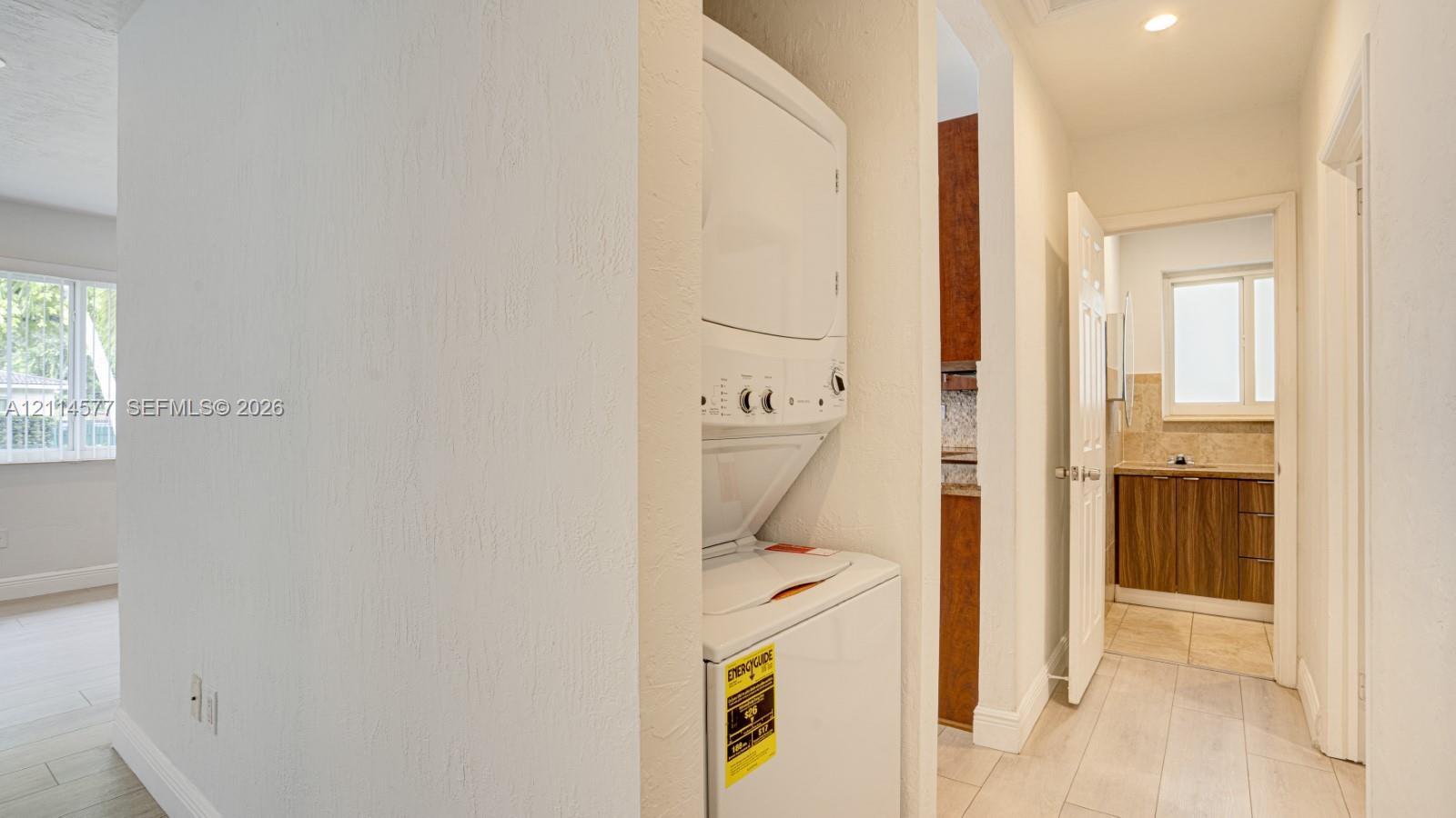 Laundry alcove featuring a stacked appliance unit, tiled flooring, and neutral wall finishes