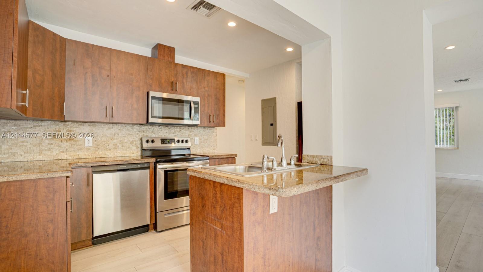 Kitchen featuring flat-panel wood cabinetry, stone countertops, textured stone backsplash, stainless steel appliances, and recessed lighting