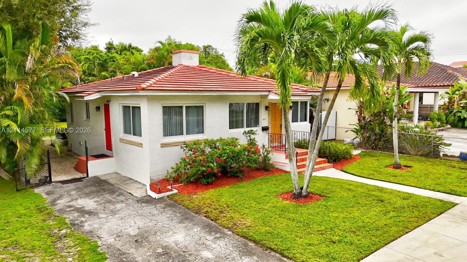 Single-story exterior featuring white stucco siding, a tiled hip roof, a concrete driveway, and mature palm landscaping