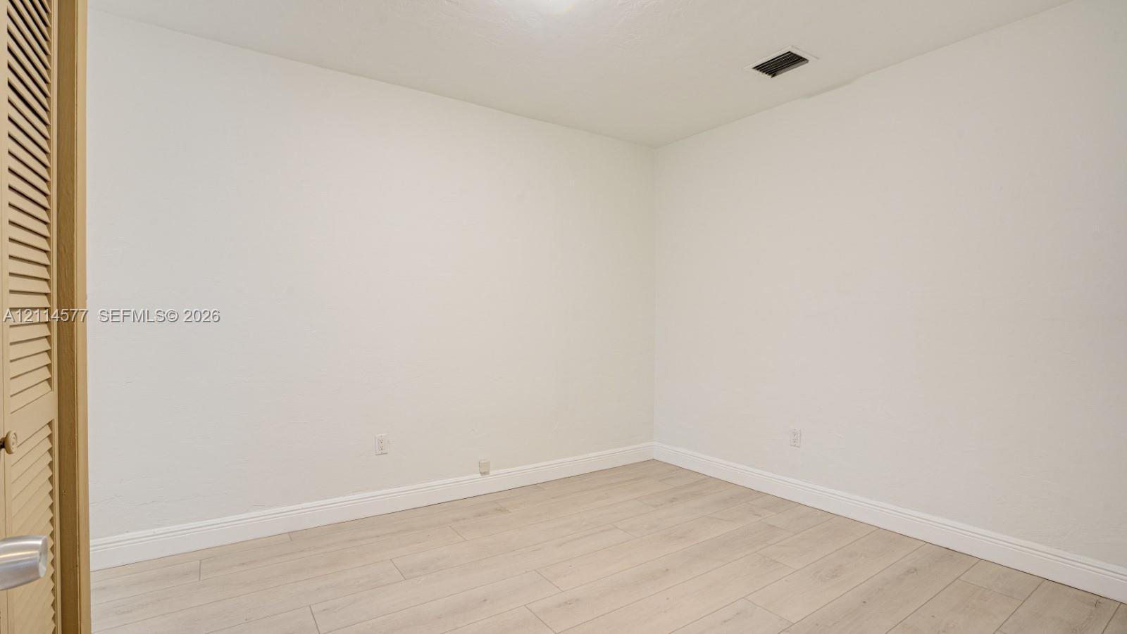 Neutral interior space featuring wood-finish flooring and louvered closet doors