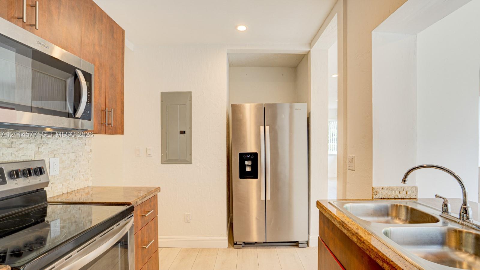 Kitchen featuring flat-panel wood-finish cabinetry, stainless steel appliances, stone countertops, textured stone tile backsplash, and a double-basin stainless steel sink with a gooseneck faucet
