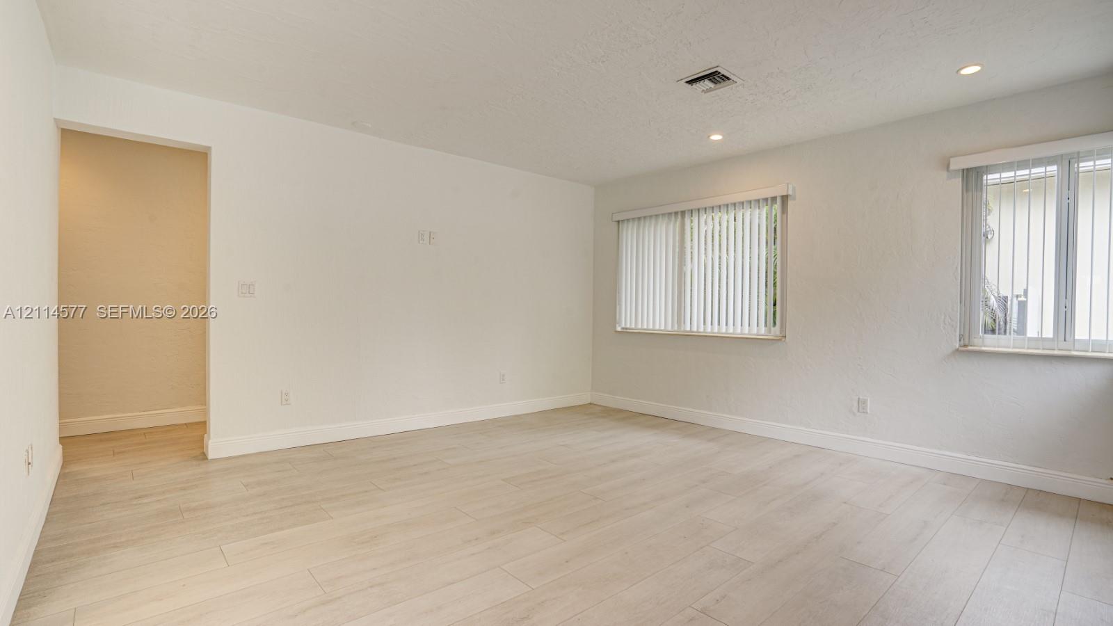 Interior space featuring light-toned wood-finish flooring, recessed lighting, and dual windows with vertical blinds