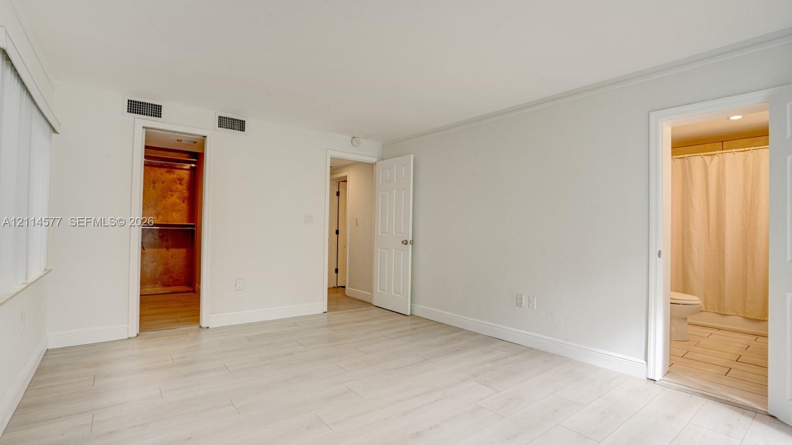 Neutral interior space featuring wood-finish flooring, recessed walk-in closet, and attached full bathroom with tile flooring