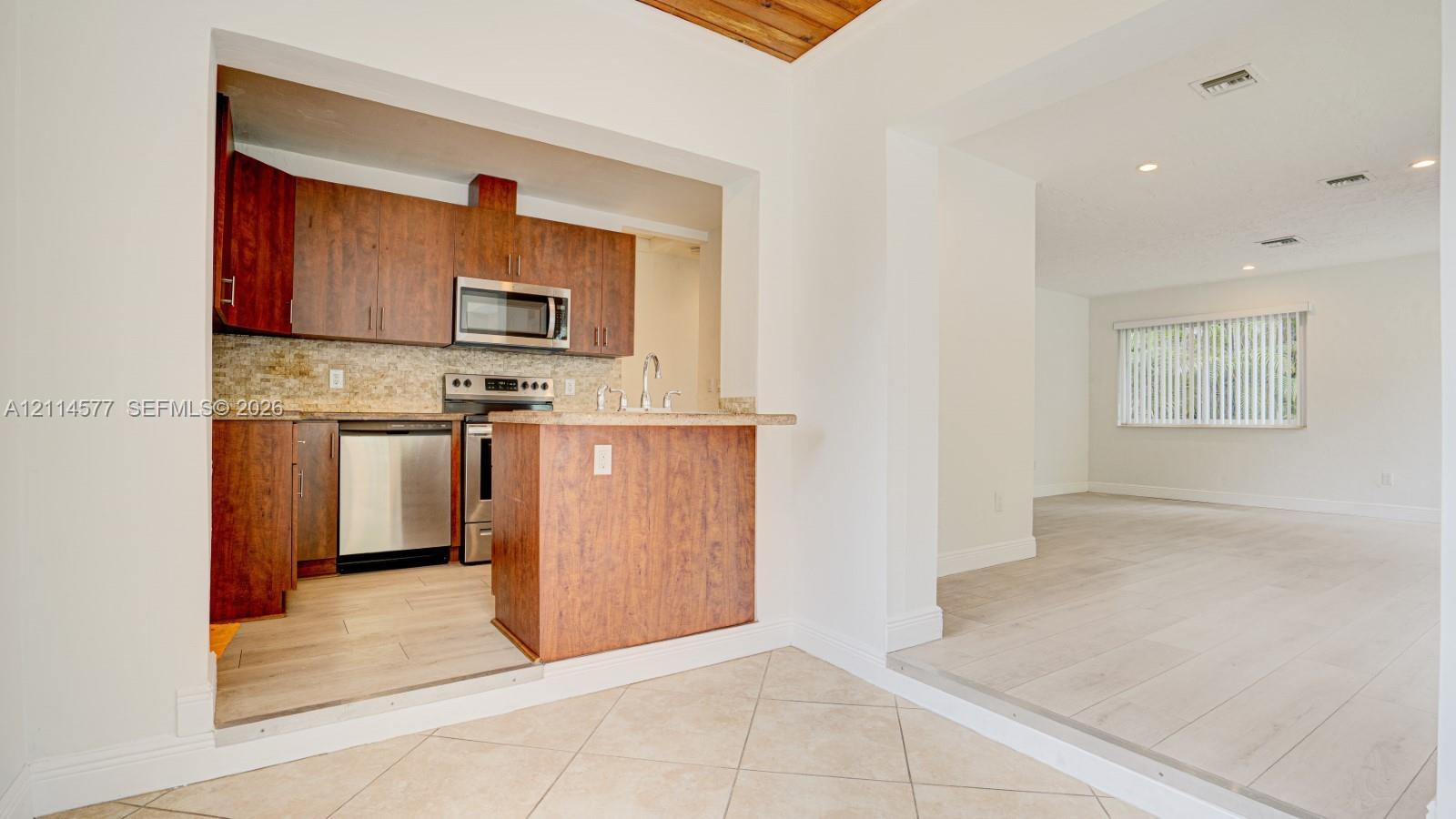 Kitchen featuring wood-finish cabinetry, stainless steel appliances, tile backsplash, and wood-finish flooring with a wood-plank ceiling accent