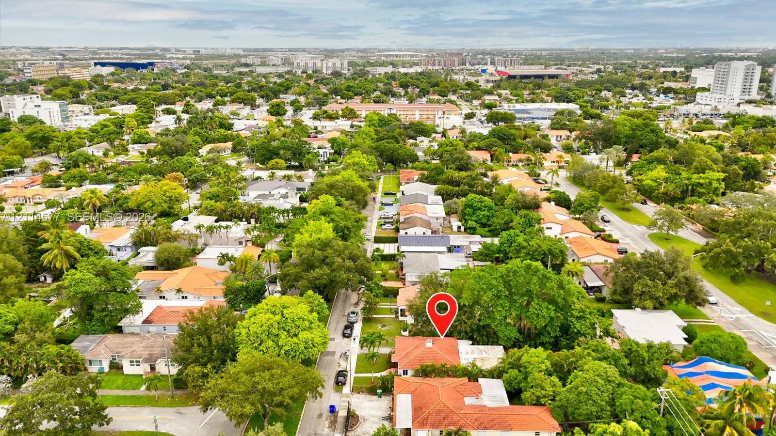 Aerial perspective featuring mature trees, paved streets, and residential density in the surrounding area
