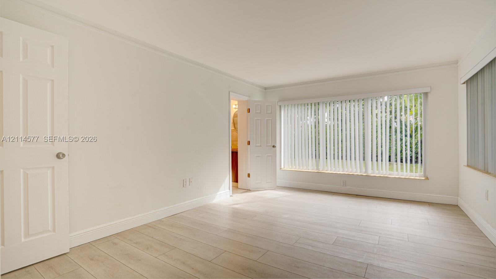 Neutral-toned interior featuring wood-finish flooring, six-panel doors, and large windows with vertical blinds