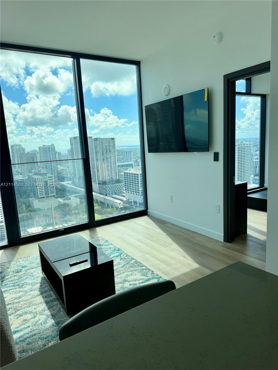Floor-to-ceiling windows with urban skyline scenery, wood-finish flooring, and black door frames