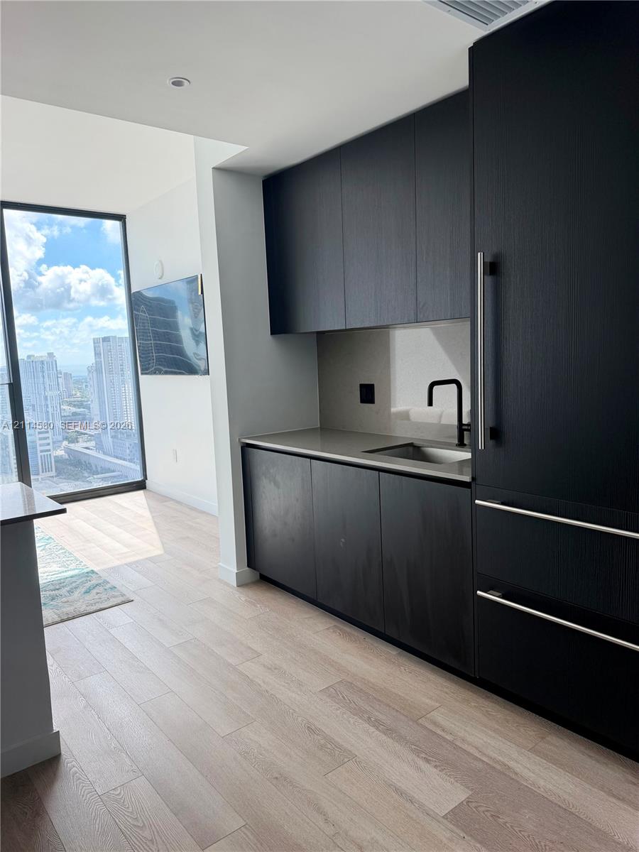 Kitchenette featuring custom matte black cabinetry, quartz countertops, a stainless steel sink with a matte black faucet, integrated appliances, and wood-finish flooring