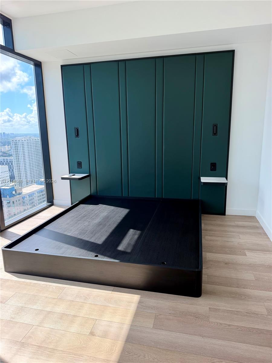 Floor-to-ceiling windows, custom emerald green paneled accent wall, wood-finish flooring, and built-in floating side shelves