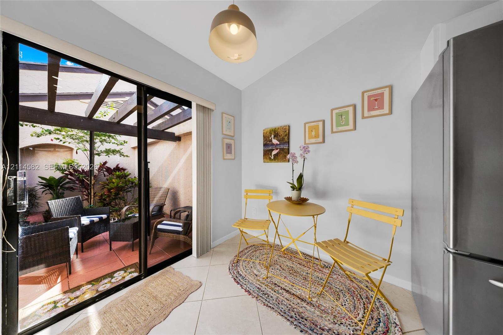 Sliding glass doors opening to a covered patio with a wooden pergola, ceramic tile flooring, and stainless steel refrigerator