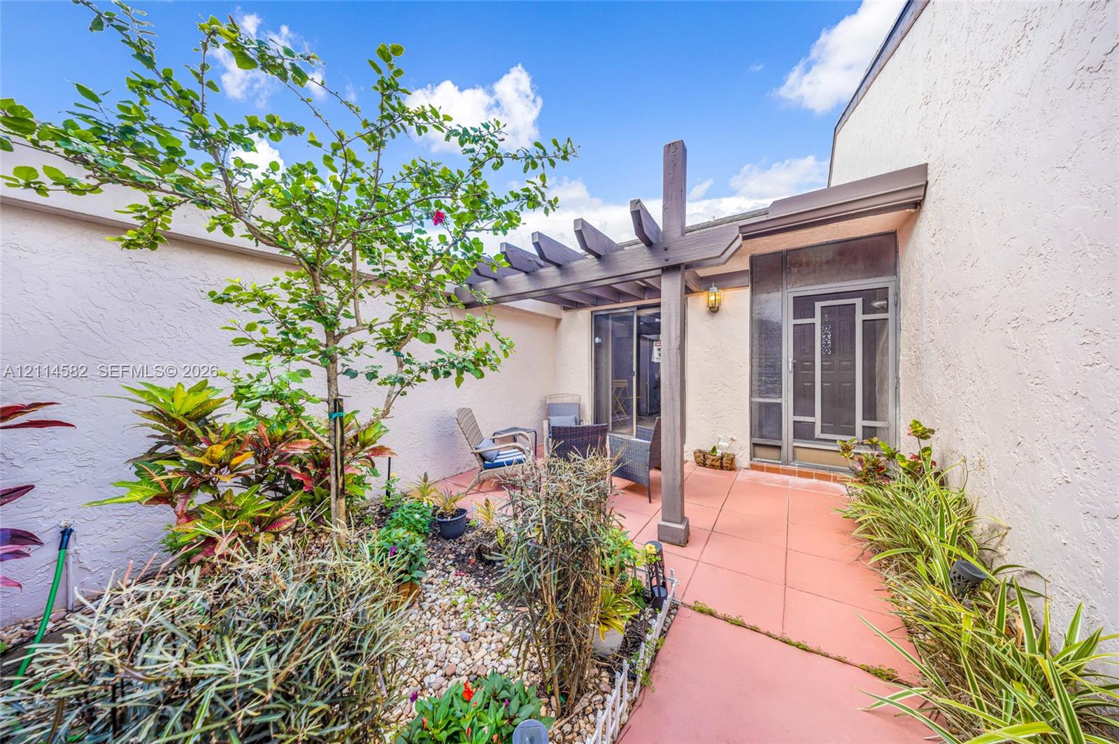 Enclosed courtyard featuring a tiled patio, custom wood pergola, xeriscaped garden beds with gravel, and a decorative screen door