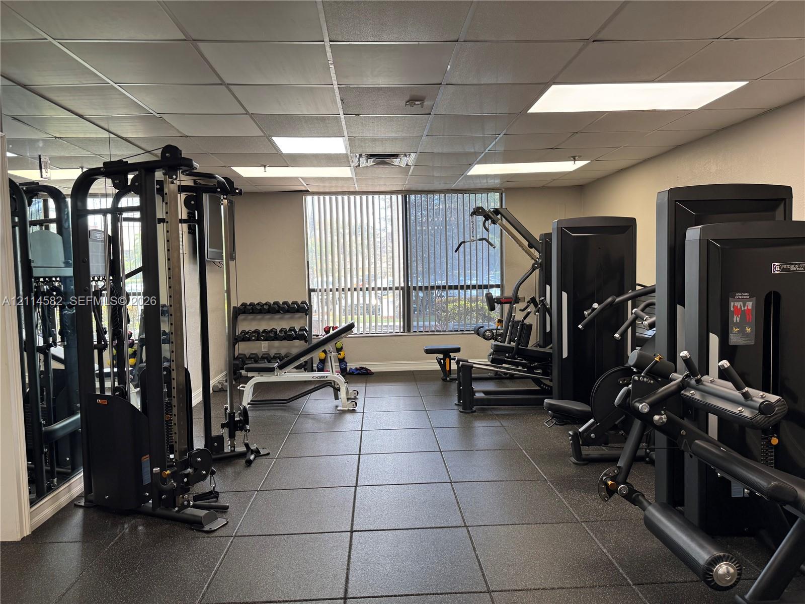 Fitness center featuring square rubber flooring, recessed drop-ceiling lighting, and wall-to-wall mirror panels