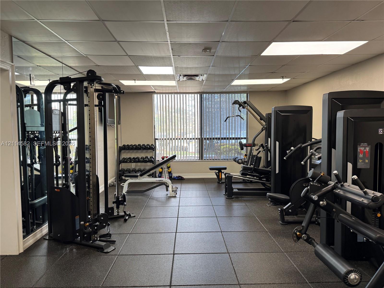 Fitness room featuring tile flooring, a mirrored wall, and floor-to-ceiling windows with vertical blinds