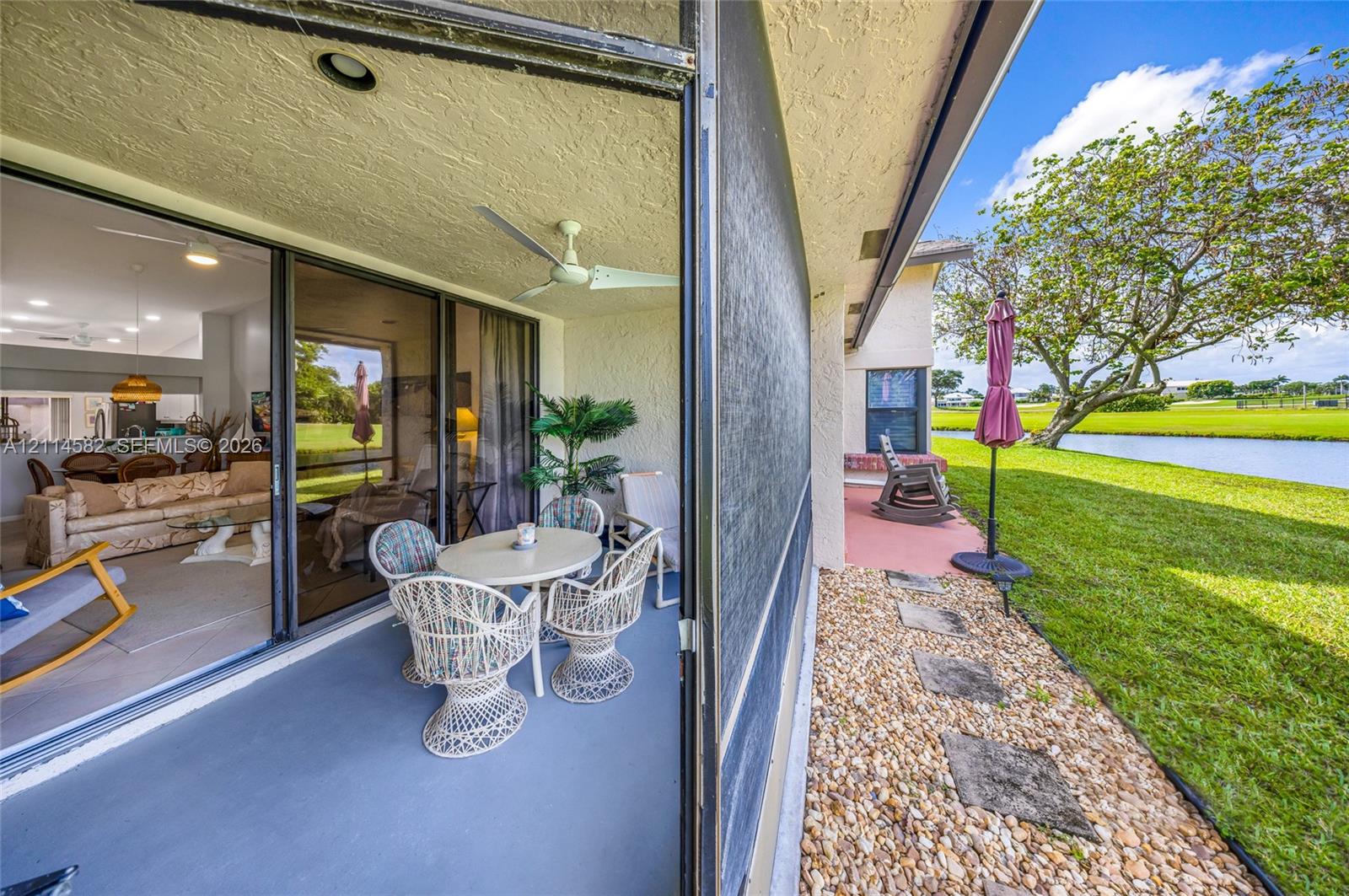 Screened lanai featuring a ceiling fan and sliding glass door, alongside a stone-paved walkway, exterior wall-mounted lighting, and water frontage