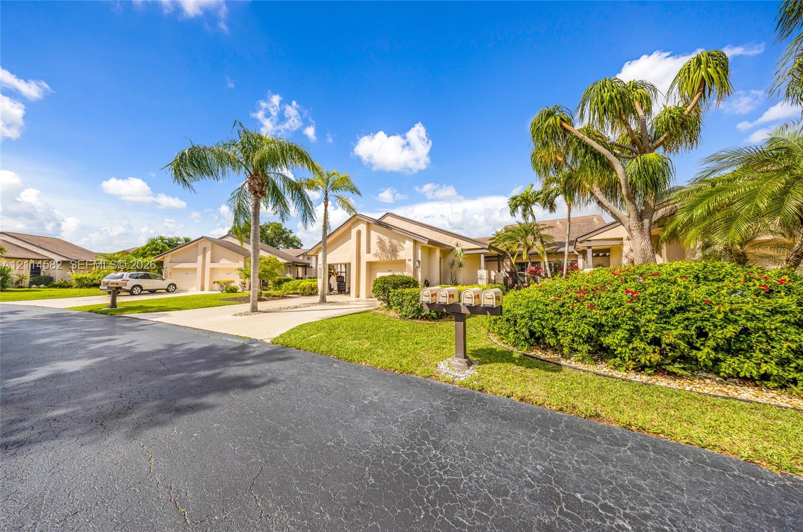 Stucco exterior featuring a low-slope roof, concrete driveway, lush landscape with mature palm trees, and manicured lawn