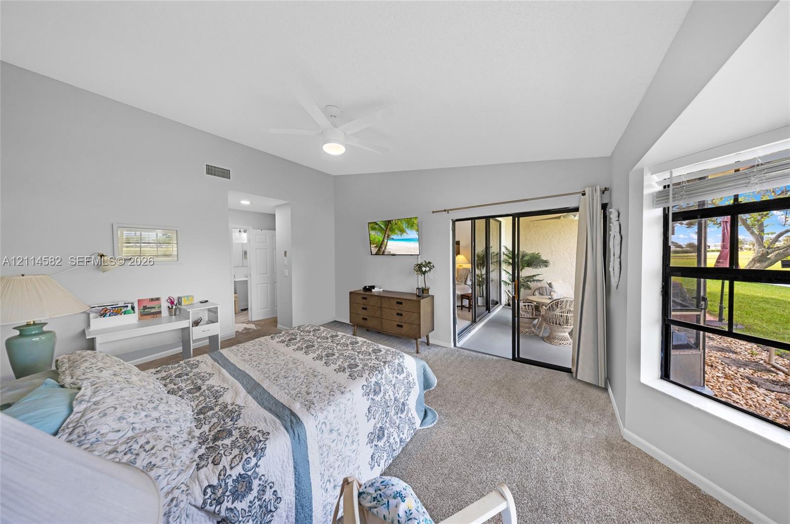 Bedroom featuring vaulted ceilings, neutral carpeting, a ceiling fan, sliding glass doors, and large windows