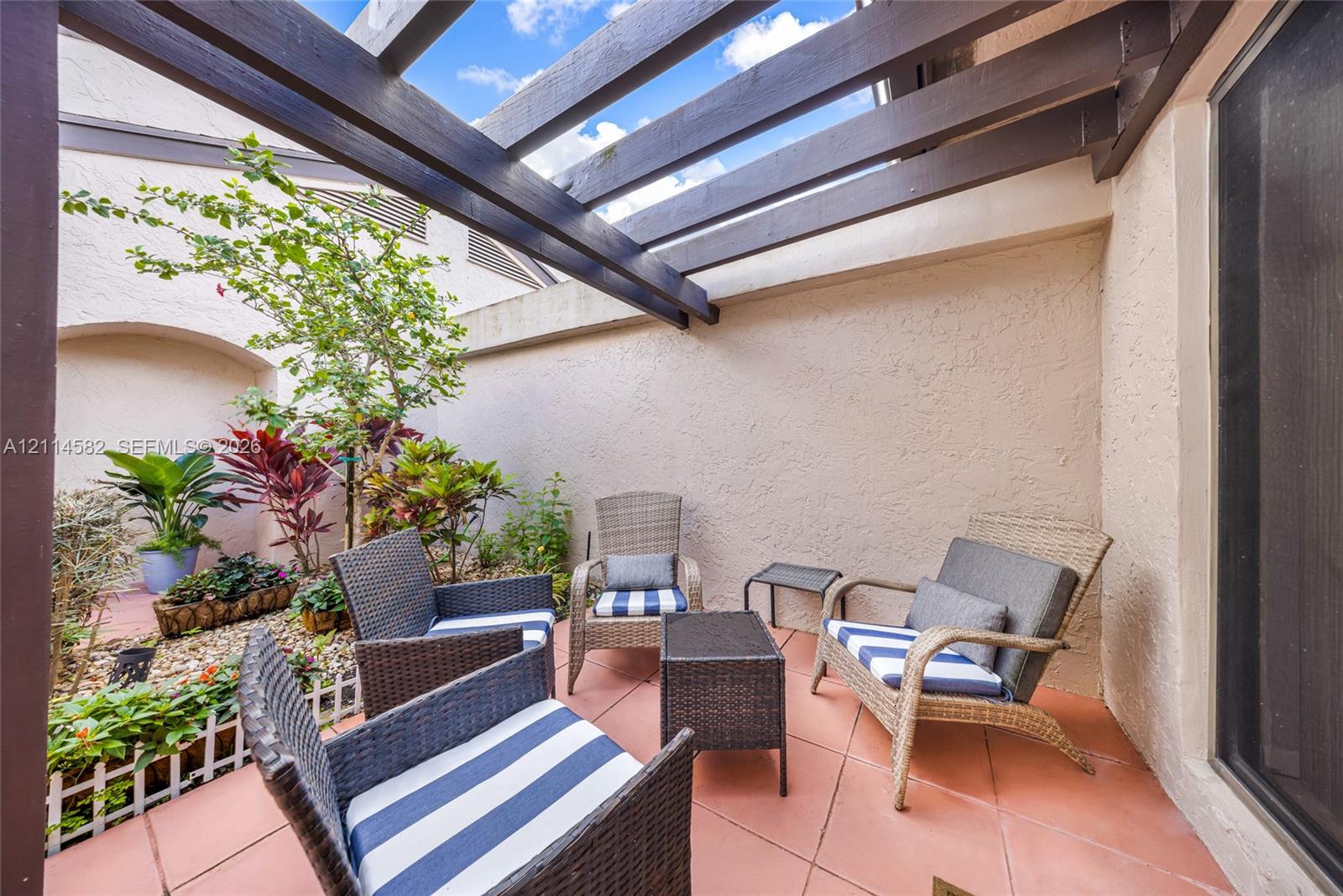 Private courtyard featuring a structural wooden pergola, ceramic tile flooring, stucco privacy walls, and low-maintenance stone landscaping