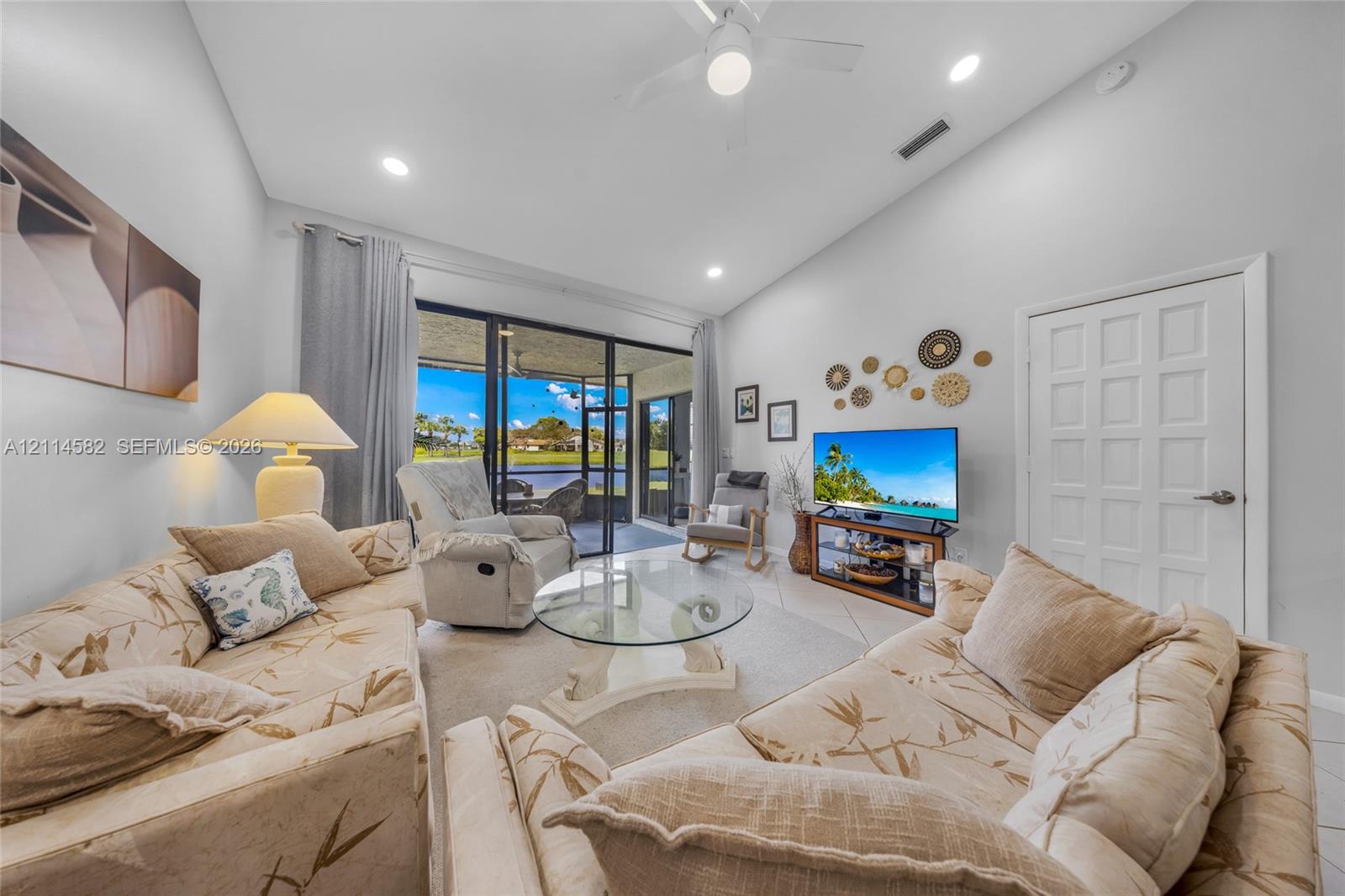 Living area featuring vaulted ceilings, recessed lighting, tile flooring, and large sliding glass doors leading to a screened-in lanai