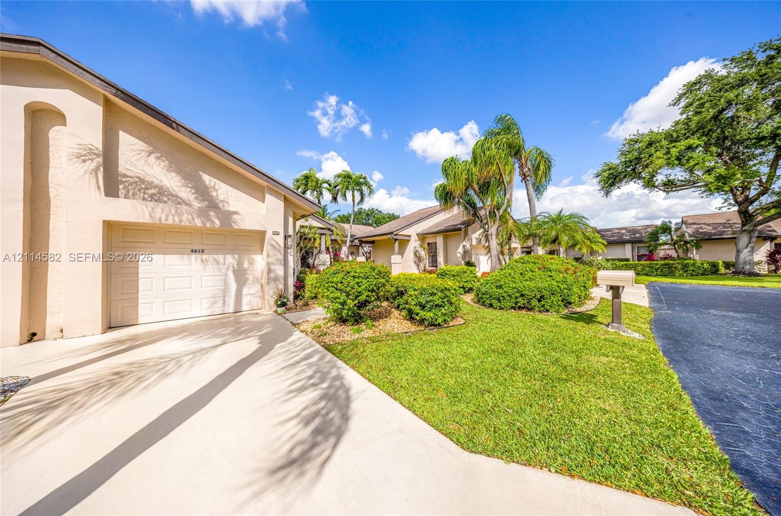 Stucco exterior featuring a paved driveway, single-car garage, manicured landscaping, and mature palm trees