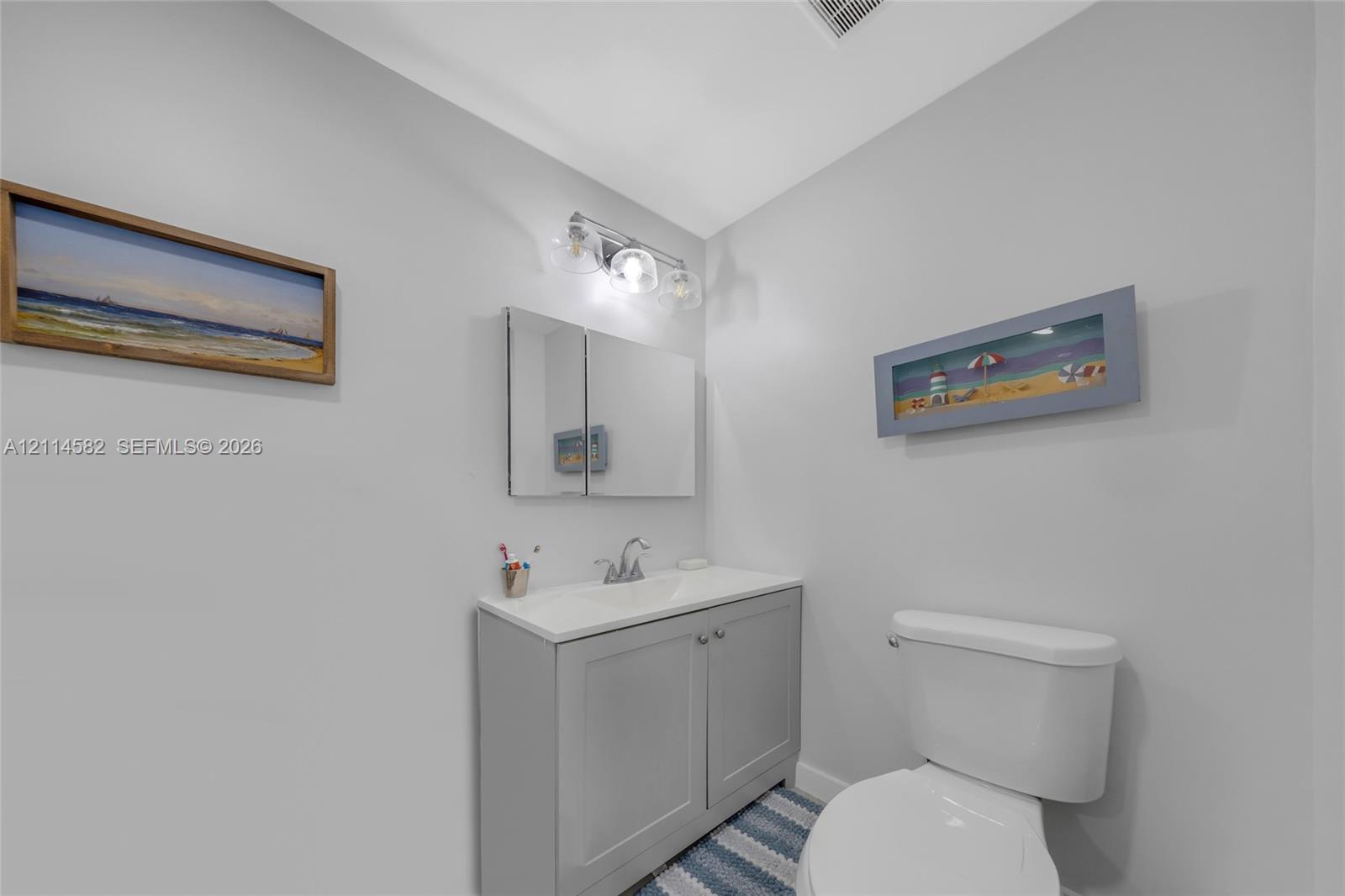 Shaker-style vanity with a solid-surface countertop, integrated basin, three-light polished chrome vanity fixture, and a mirrored medicine cabinet
