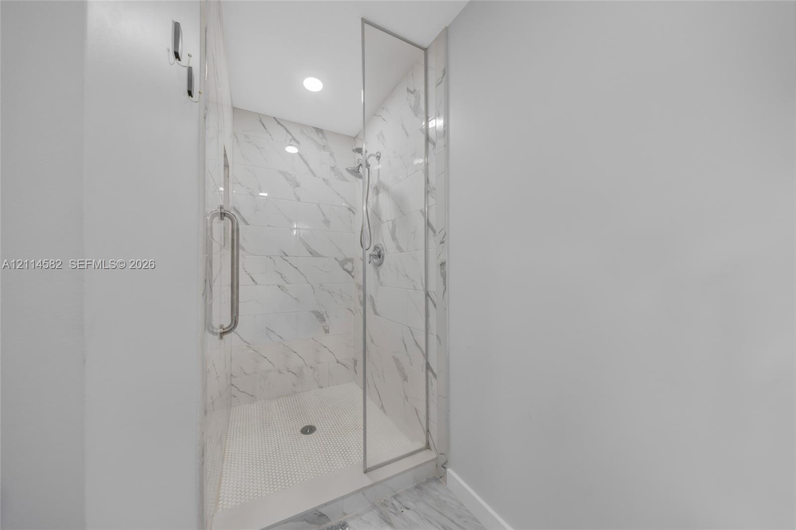 Walk-in shower featuring floor-to-ceiling stone-finish tile surround, frameless glass door, metallic hardware, and mosaic tile shower floor