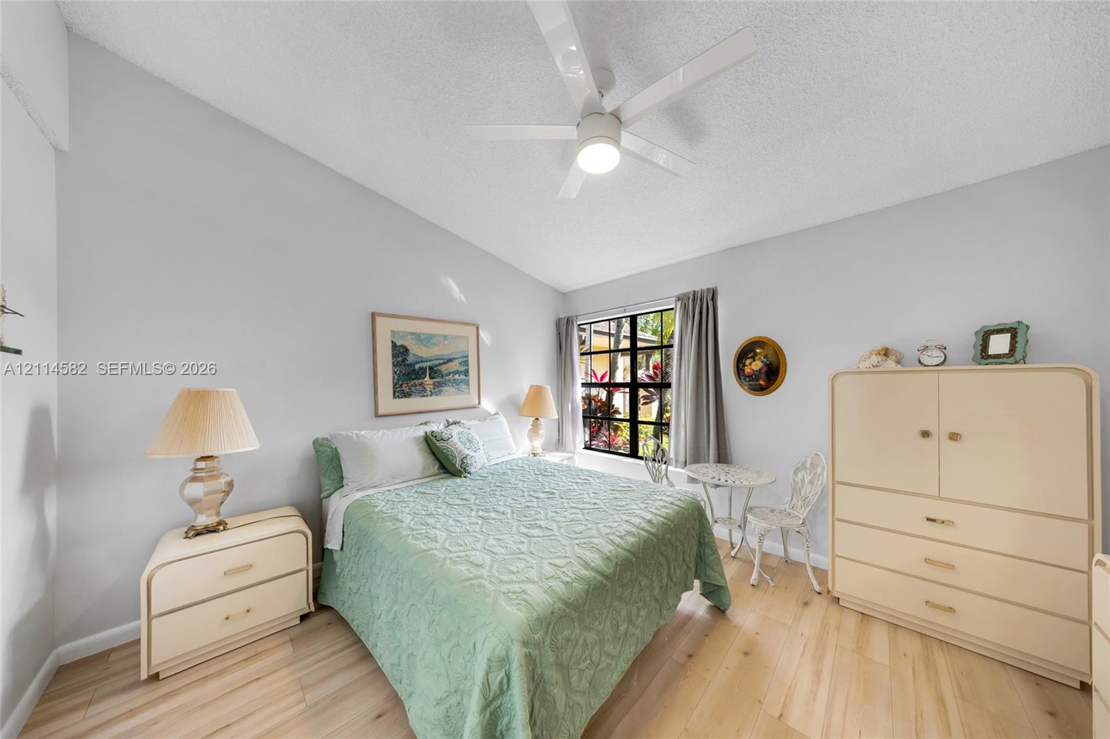 Neutral-toned interior featuring wood-finish flooring, a white multi-blade ceiling fan with integrated lighting, and a window with black-framed casing