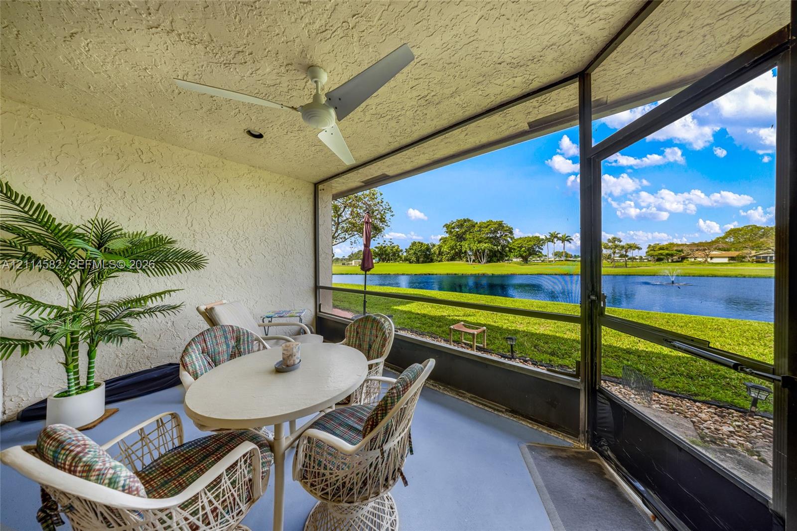 Screened-in lanai featuring a solid-surface floor, ceiling-mounted fan, and floor-to-ceiling screens overlooking a pond and manicured lawn