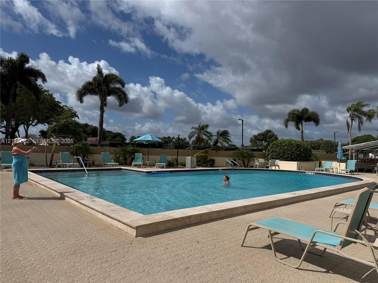 In-ground swimming pool featuring a concrete surround, light-toned stone coping, and perimeter privacy wall