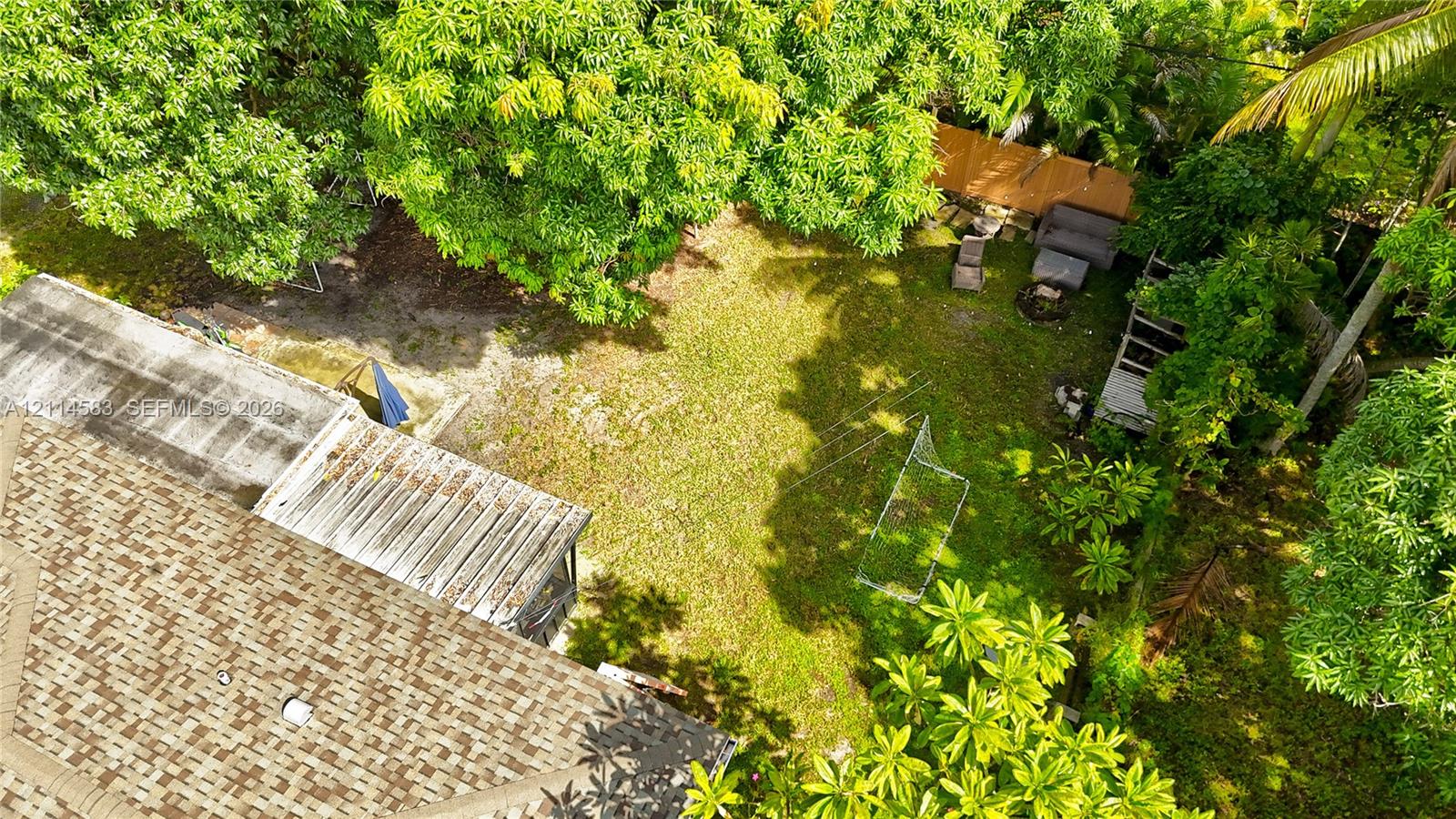 Expansive backyard featuring mature tree canopy, wood-panel fencing, and a shingle-roof structure