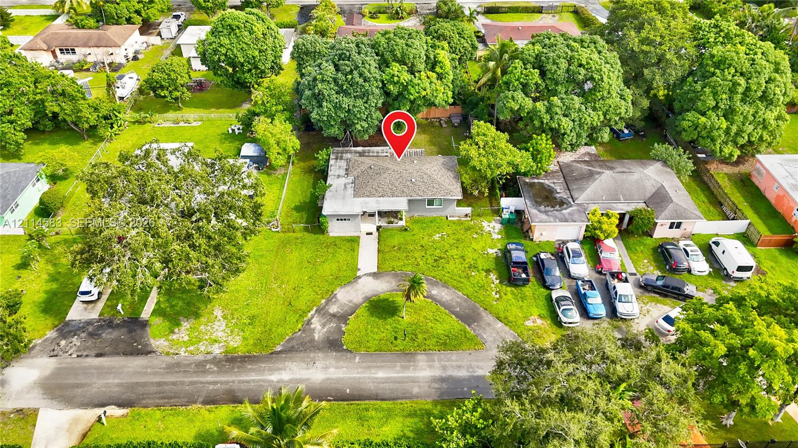 Aerial perspective of a property featuring a hip-roof structure, a circular driveway, and mature landscaping on a spacious lot