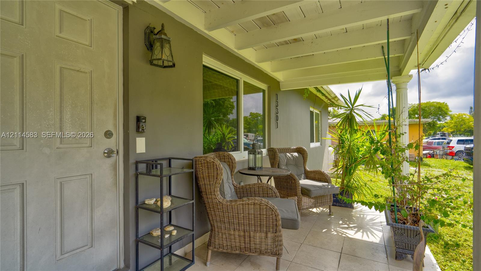 Covered front porch featuring tile flooring, exposed beam ceiling, decorative column, and wall-mounted exterior lighting