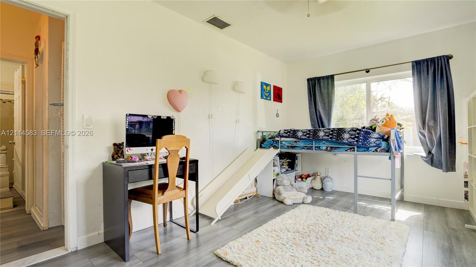 Room featuring wood-finish flooring, dual wall-mounted light fixtures, and a window with a curtain rod