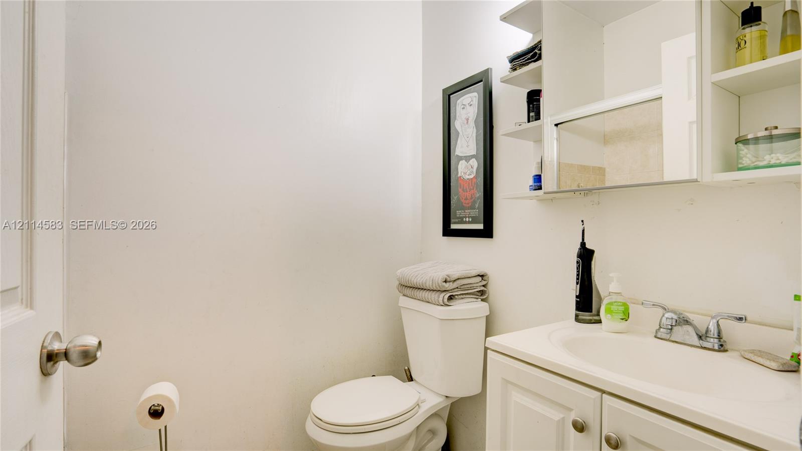 White vanity cabinet featuring an integrated sink, polished chrome dual-handle faucet, and overhead cabinetry with built-in shelving and mirror