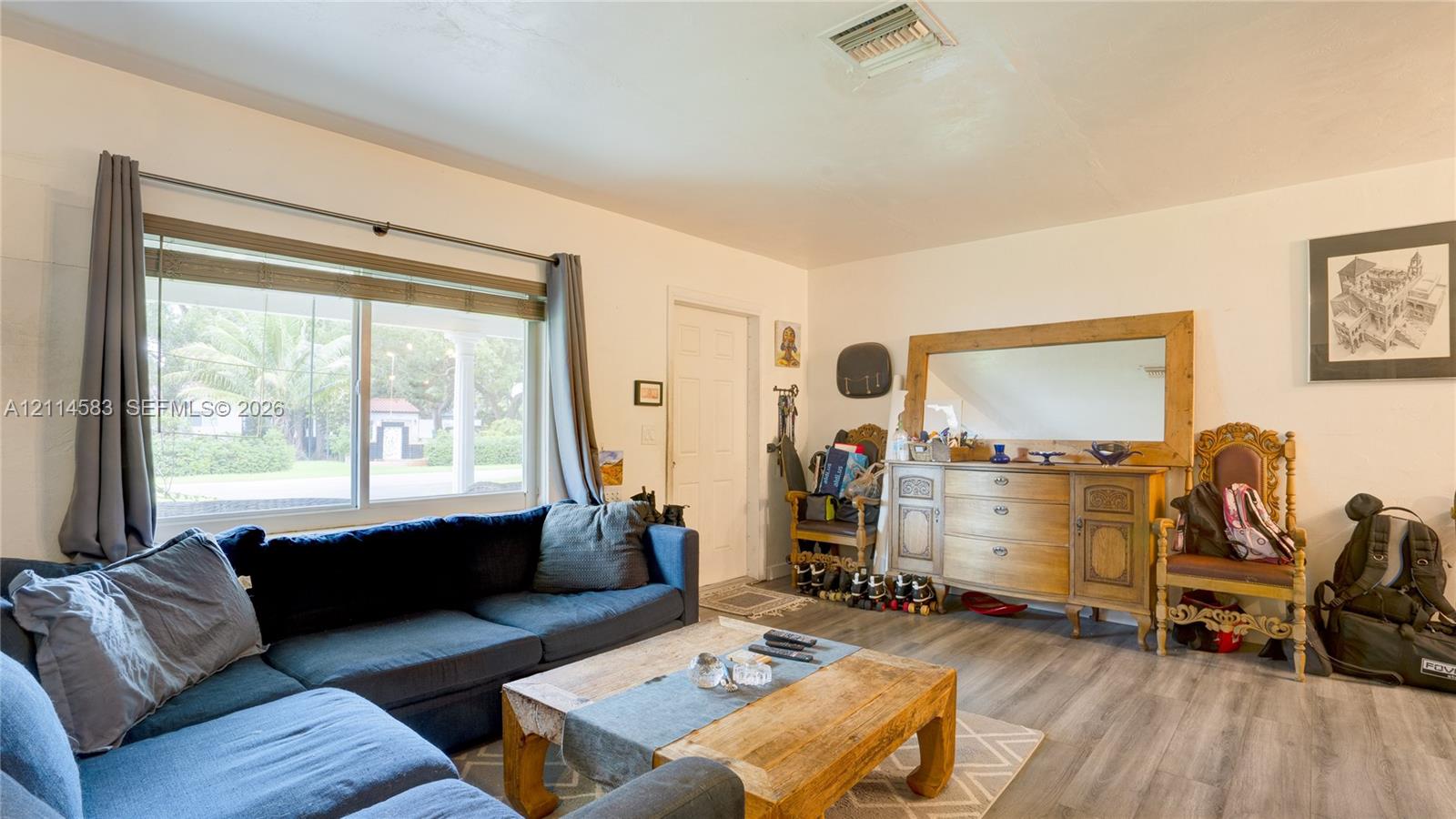 Living area featuring large window with natural light, wood-finish flooring, and crisp white wall finish
