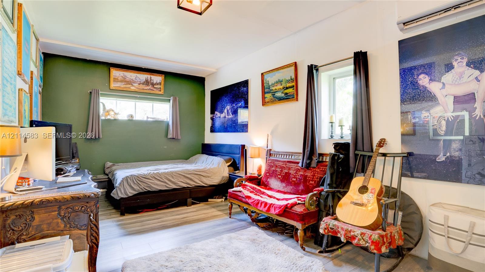 Room featuring wood-finish flooring, two windows with horizontal panes, an olive green accent wall, and an overhead lighting fixture