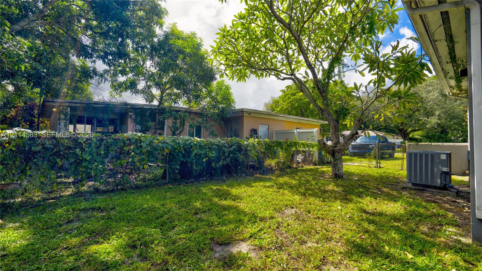 Exterior grounds featuring a spacious lawn, mature trees, a chain-link fence, and an exterior HVAC unit