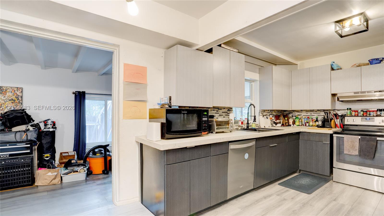 Kitchen featuring two-tone flat-panel cabinetry, light-toned stone-finish countertops, multi-colored linear tile backsplash, stainless steel dishwasher, and wood-finish flooring