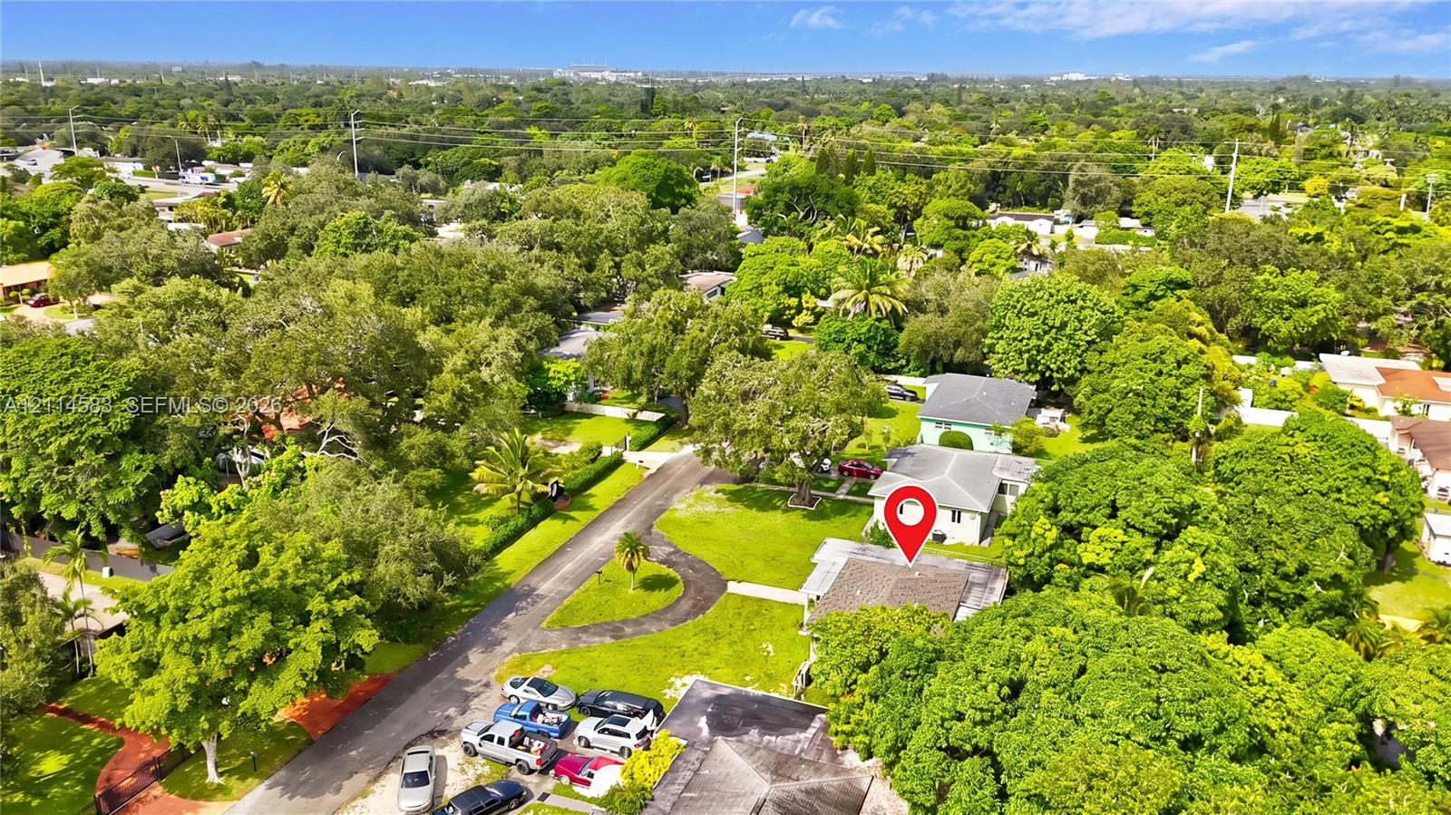 Aerial perspective featuring mature trees, manicured lawns, asphalt driveway, and residential surroundings