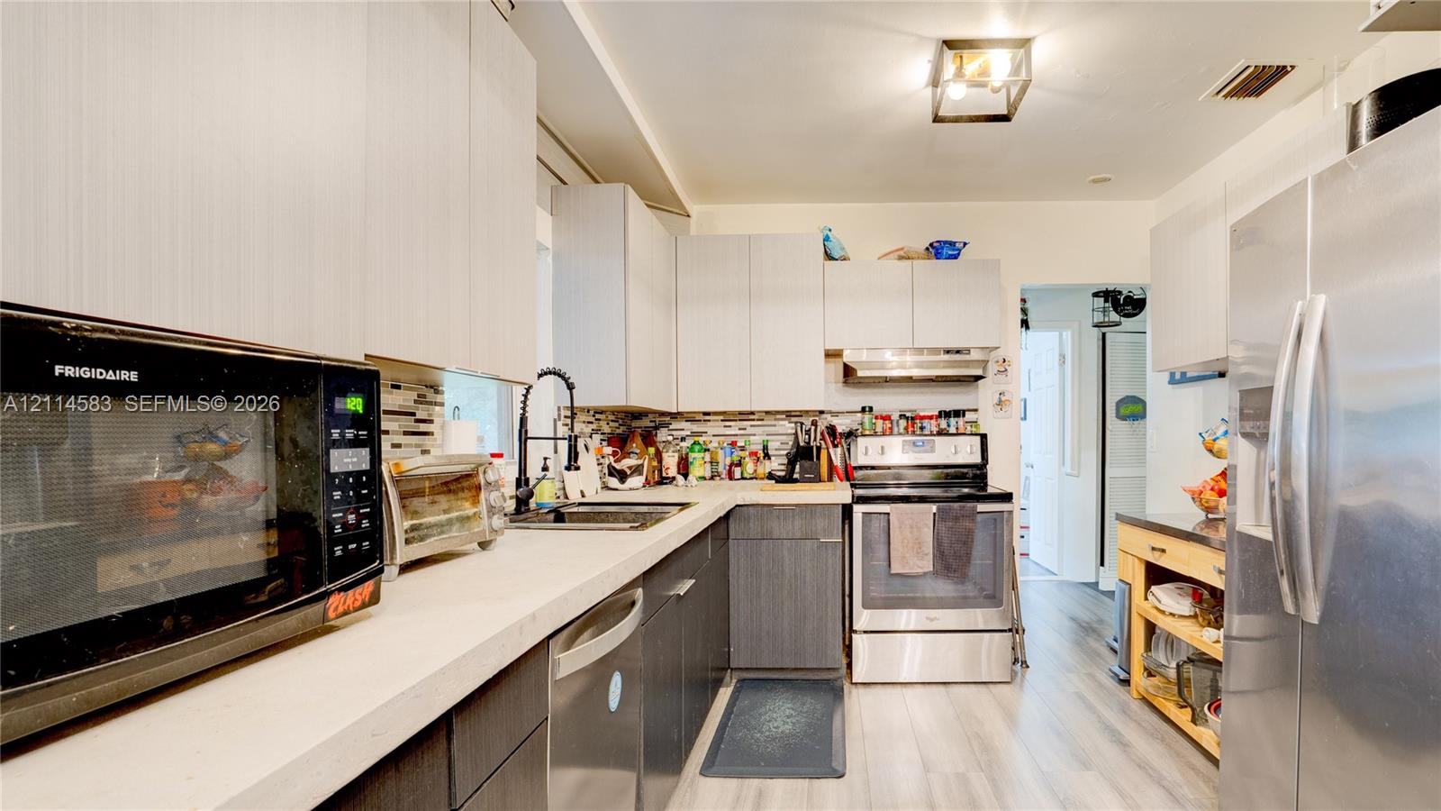 Kitchen featuring flat-panel cabinetry, light-toned countertops, multi-material tile backsplash, stainless steel appliances, and wood-finish flooring