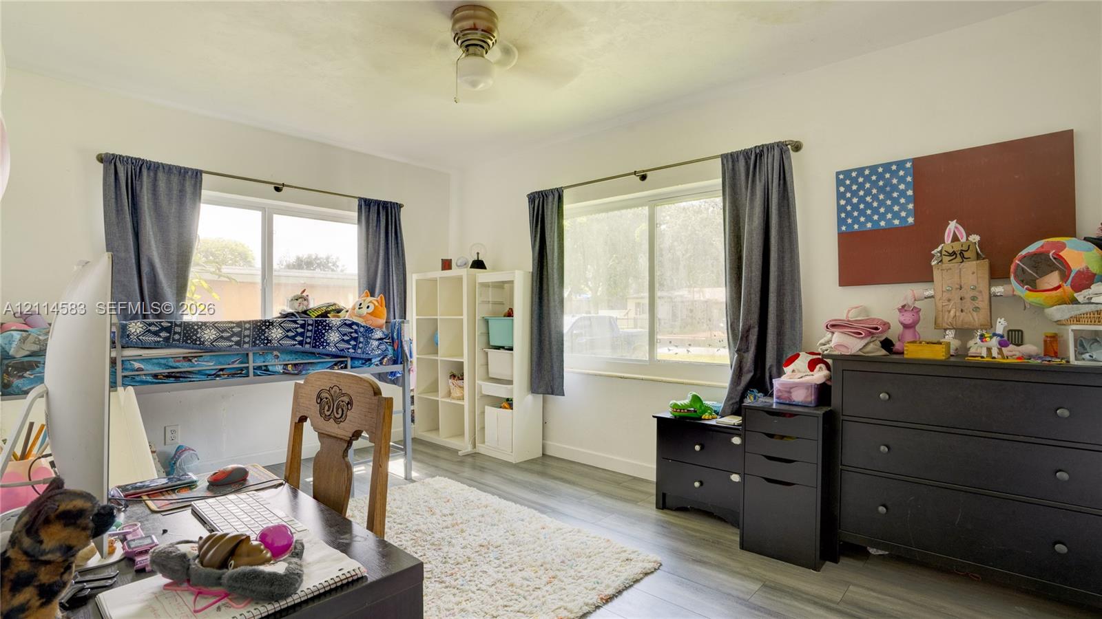 Room featuring wood-finish flooring, two large sliding windows, and a central ceiling fan