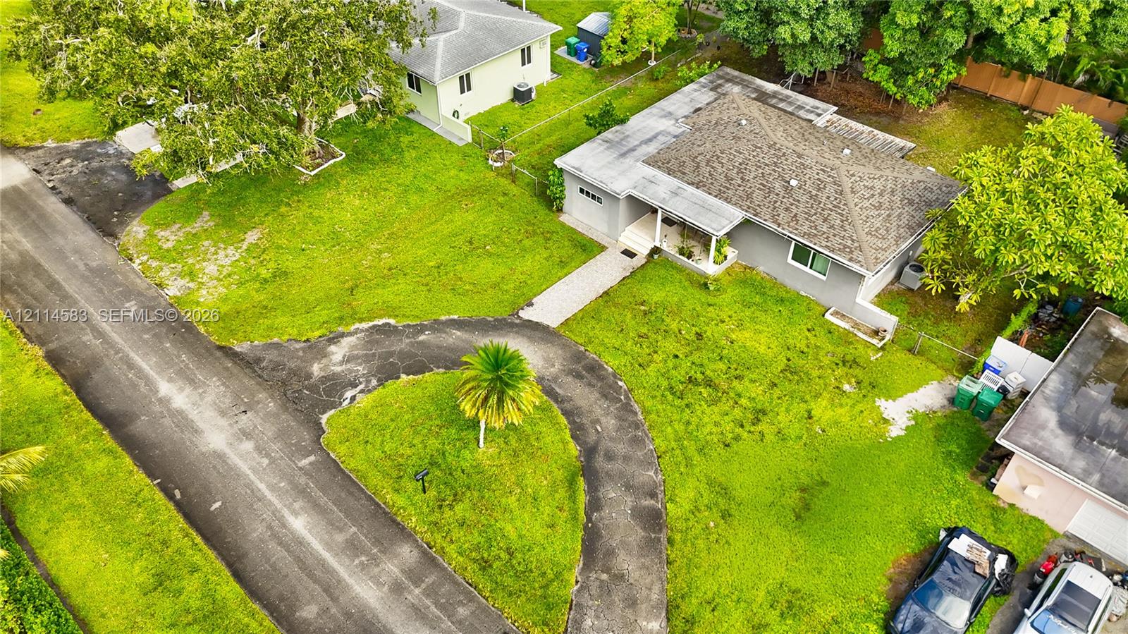 Aerial perspective featuring a single-story residence with a pitched shingle roof, a curved asphalt driveway, and expansive lawn space Aerial perspective featuring a single-story residence with a pitched shingle roof, a curved asphalt driveway, and expansive lawn space