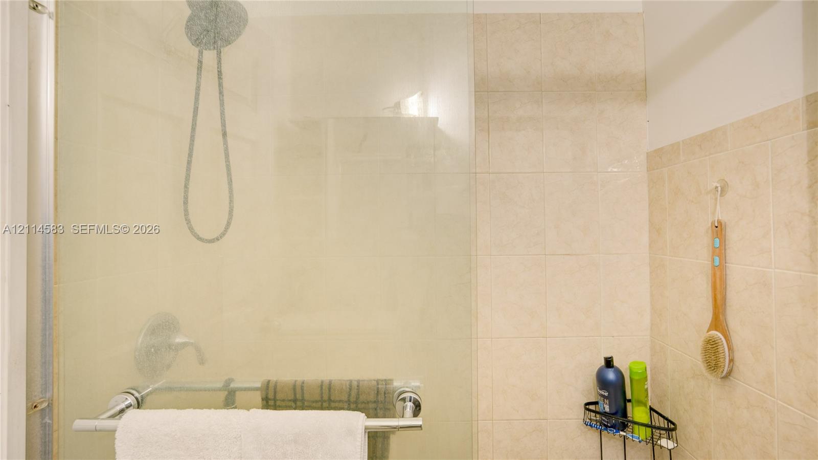 Walk-in shower featuring a frameless glass enclosure, polished chrome rainfall showerhead, wall-mounted control valve, and neutral tile wall surround