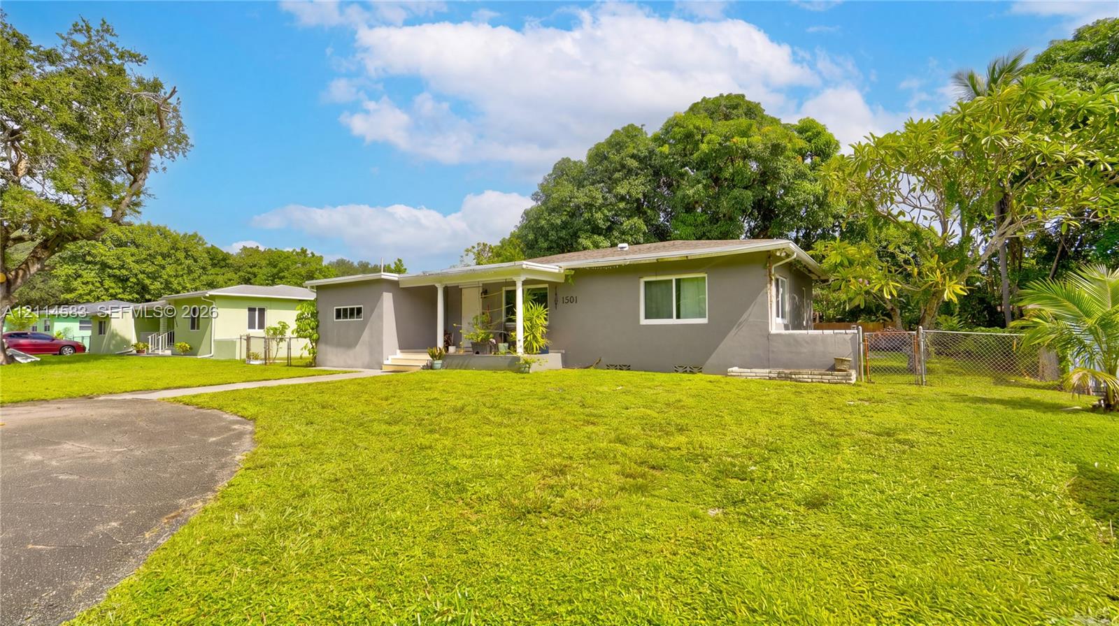 Single-story exterior featuring a gray stucco facade, covered porch entry, asphalt driveway, and expansive lawn with mature landscaping Single-story exterior featuring a gray stucco facade, covered porch entry, asphalt driveway, and expansive lawn with mature landscaping