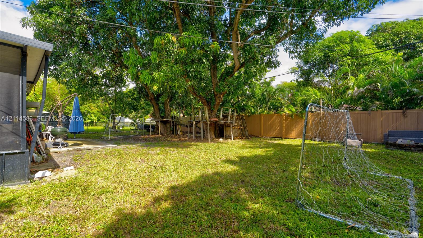 Backyard featuring a privacy fence, mature trees, and a concrete patio