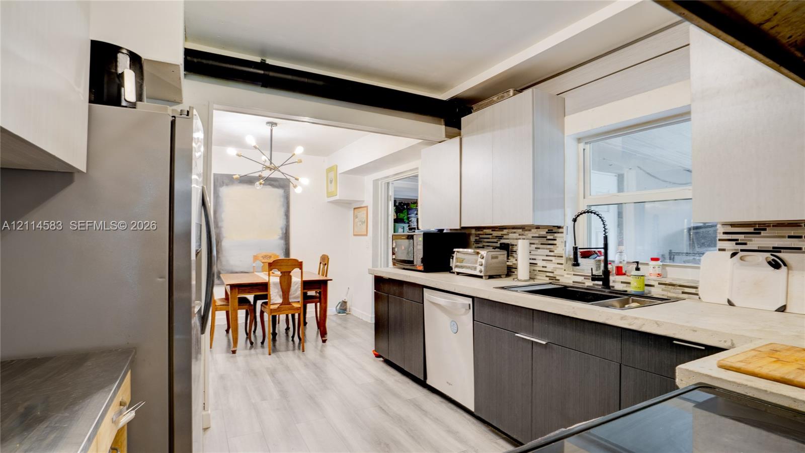 Kitchen featuring dual-tone cabinetry, stone-finish countertops, linear tile backsplash, stainless steel appliances, and a gooseneck faucet