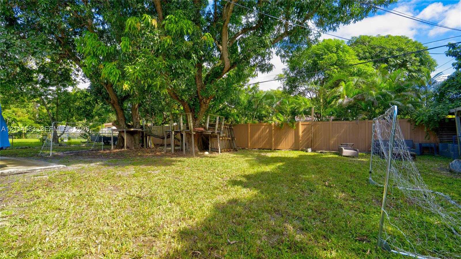 Expansive backyard featuring mature tree canopy, integrated wooden platform structure, and solid perimeter fencing