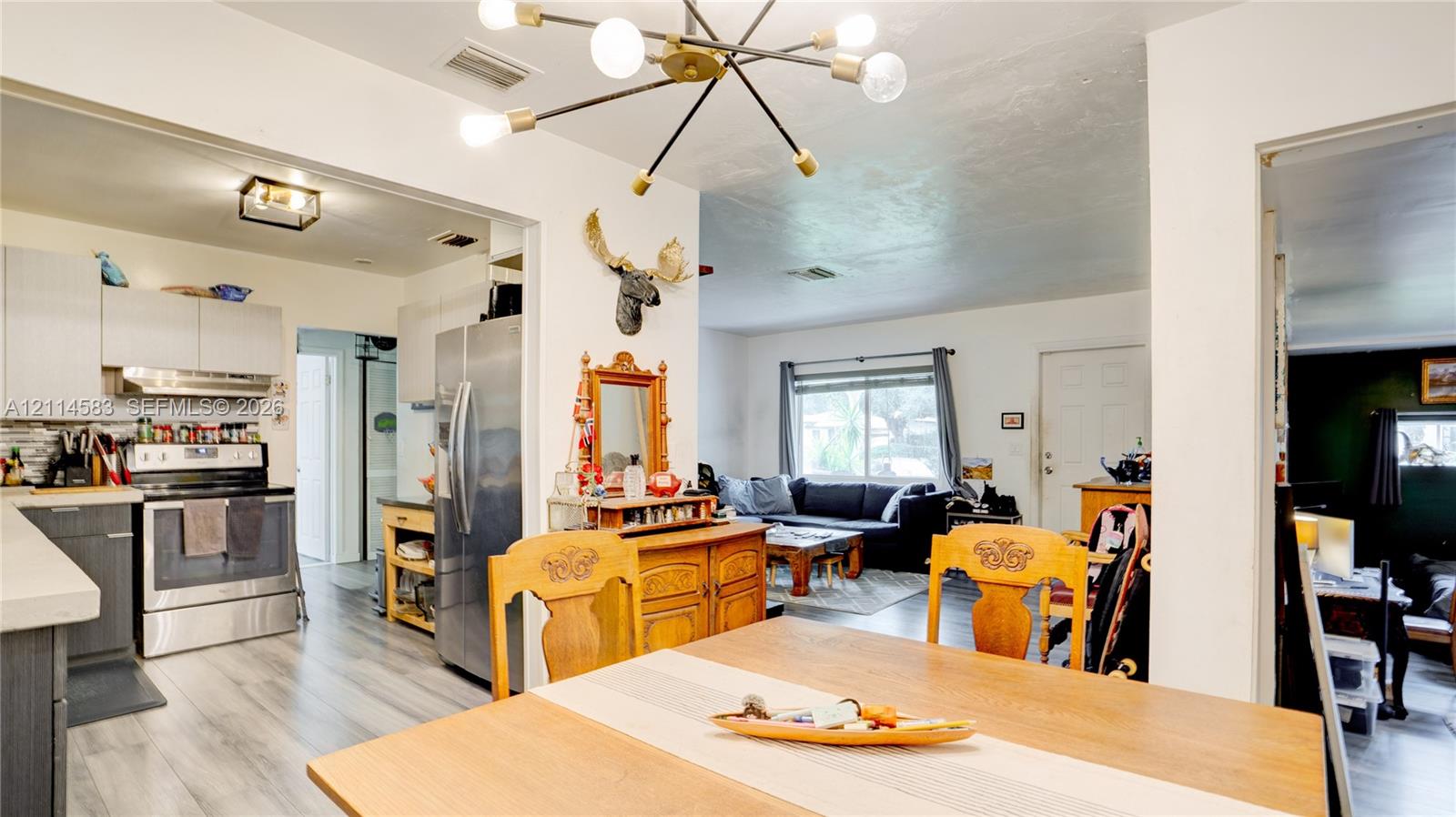 Kitchen featuring stainless steel appliances, flat-panel cabinetry, and light-toned wood-finish flooring, illuminated by a multi-arm modern sputnik chandelier