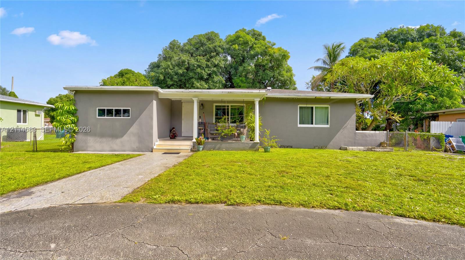 Single-story exterior featuring a gray stucco facade, covered front porch with support columns, concrete driveway, and expansive lawn Single-story exterior featuring a gray stucco facade, covered front porch with support columns, concrete driveway, and expansive lawn