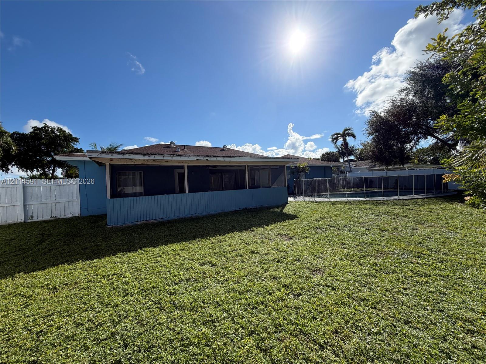 Rear exterior featuring a screened patio, private pool with mesh enclosure, and perimeter vinyl fencing
